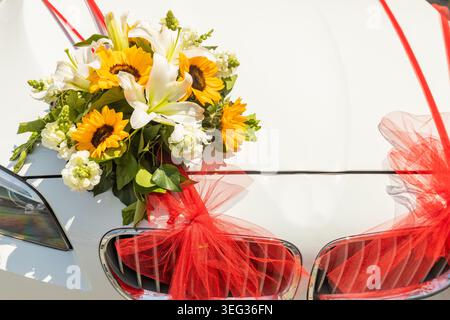Horizontaler Blick auf ein luxuriöses weißes Hochzeitsauto mit frischen Blumen und roten Bändern. Nahaufnahme Stockfoto