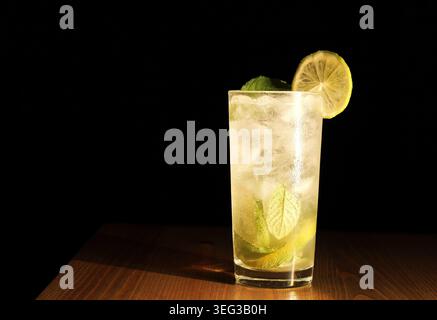 Erfrischender Mojito-Cocktail mit Limettenkeilen, verwirrter Minze und Eis in einem hohen Glas auf einem Holztisch, kühles sprudelndes Rum-Getränk perfekt für Sommer, Bar oder Stockfoto