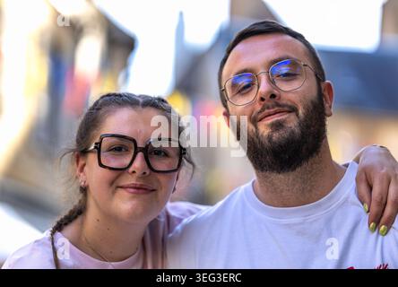 Dijon, Frankreich - 9. Mai 2026: Ein junger Mann und eine elegant gekleidete Frau unterhalten sich auf einem Bürgersteig im Stadtzentrum. Ein Pett teilen Stockfoto
