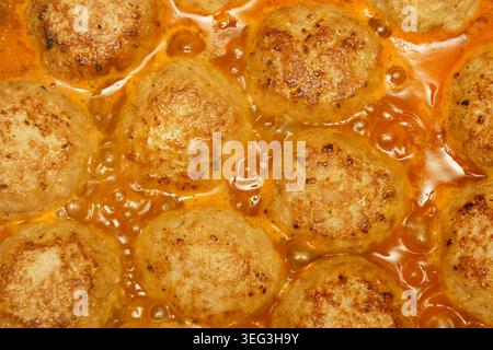 Fleischbällchen köcheln in einer reichhaltigen Sauce auf dem Herd in einer Küche. Die Hitze erzeugt Blasen um das Fleisch herum, die den Kochvorgang zeigen. Stockfoto