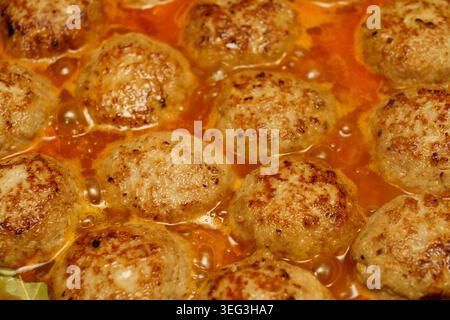 Fleischbällchen kochen in einem Topf mit Soße. Die Küche ist warm und mit der Zubereitung von Speisen beschäftigt. Stockfoto