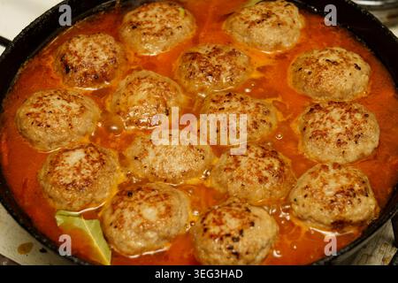 Frikadellen, die in Tomatensoße auf einem Herd in einer Kücheneinrichtung garen Stockfoto