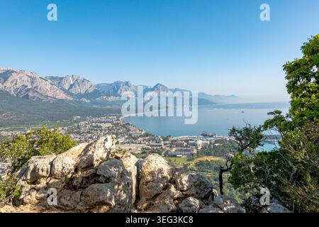 Blick auf Kemer von einem Hügel in der Nähe der Stadt. Blick auf das Mittelmeer an einem sonnigen Morgen im Mai. Steine und Bäume im Vordergrund Stockfoto