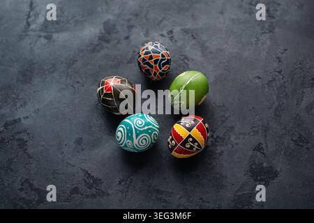 Fünf traditionelle ukrainische Pysanky-Ostereier mit geometrischen und floralen Mustern auf dunkelgrauer Oberfläche. Ansicht von oben: Handgemalte ukrainische Pysanky. Stockfoto