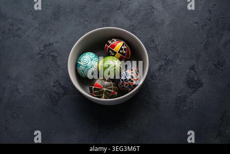 Fünf traditionelle ukrainische Pysanky-Ostereier mit geometrischen und floralen Mustern in einer grauen Schüssel. Blick von oben auf handbemalte ukrainische Pysanky-Eier. Stockfoto