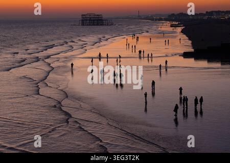 Silhouetten von Menschen am Strand bei Ebbe, Brighton & Hove, East Sussex, England, Großbritannien. Die senkrechten Säulen dahinter auf der rechten Seite stellen die Überreste des alten West Pier dar. Stockfoto