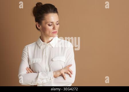 Eine professionelle Frau in einer weißen Bluse steht mit überkreuzten Armen und blickt mit einem besinnlichen oder besorgten Ausdruck nach unten, tief in Gedanken. Stockfoto