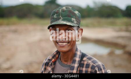 Lächelnder asiatischer Mann mit Camouflage-Mütze, der im Freien echtes Glück zeigt Stockfoto