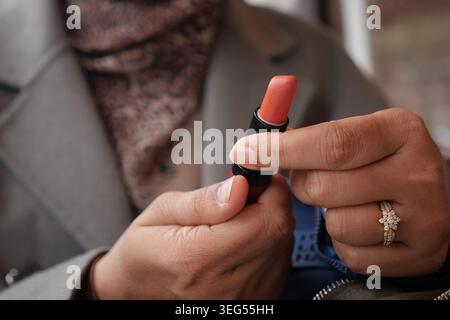 Frau, die Lippenstift aufträgt, während sie eine Tube Make-up hält Stockfoto