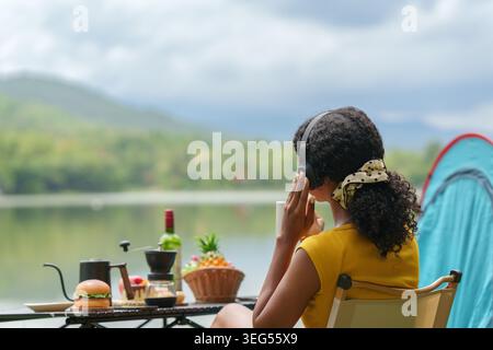 Schwarze Frau, die Musik mit Kopfhörern hört, während sie am See campt Stockfoto