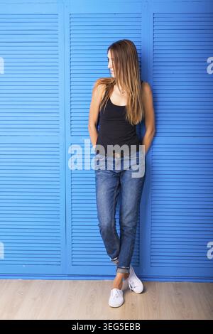 Lächelnde positive emotionale Frau, die vor blauem Hintergrund steht Stockfoto