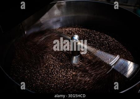 Eine Nahaufnahme der gerösteten Kaffeebohnen, die sich in einer kreisförmigen Bewegung in der Metallkühlschale eines professionellen Industrierösters drehen. Stockfoto