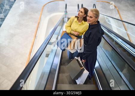 Erwachsene Frauen, die Einkaufstaschen auf dem Escalator in der Mall tragen Stockfoto
