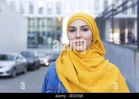 Schöne arabische muslimische Frau trägt gelbe Hijab, stilvolle weibliche Gesicht Porträt über Stadt Straße Stockfoto