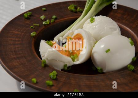 Weich gekochte Eier mit grüner Zwiebel, serviert auf rustikalem Holzteller Stockfoto
