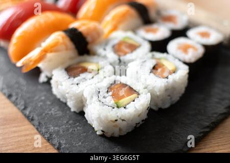 Frisches Sushi-Sortiment mit Lachs-Maki und Nigiri auf schwarzem Schieferbrett Stockfoto