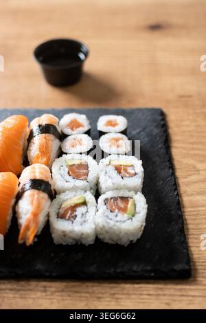 Frisches Sushi-Sortiment mit Lachs-Maki und Nigiri auf schwarzem Schieferbrett Stockfoto