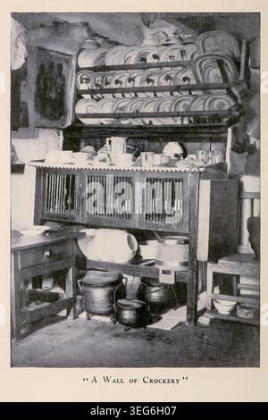 In der Küche befindet sich eine große Sammlung von Tellern, Schüsseln und Töpfen auf offenen Regalen, in einem Holzschrank und auf dem Boden, die traditionelle Haushaltsaufbewahrung widerspiegeln. Aus The Land of Heather von Clifton Johnson, 1865-1940 Publikationsdatum 1903 Stockfoto