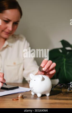 Persönliches Finanzierungskonzept mit einer Frau, die Münzen in eine Sparkasse steckt Stockfoto