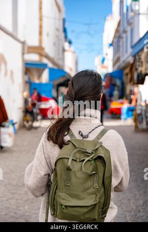 Frau mit Rucksack geht durch den marokkanischen Straßenmarkt in Essaouira Stockfoto