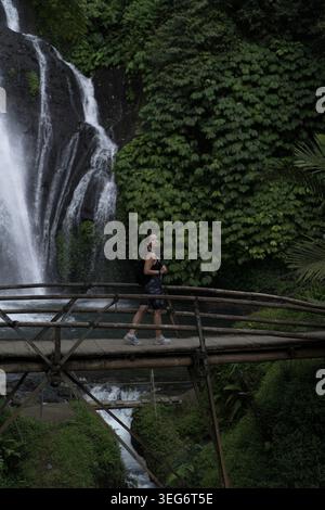 Aktive Frau, die auf der Bambusbrücke am Banyumala Wasserfall auf Bali läuft Stockfoto