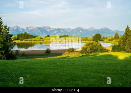 Deutschland, Kristallsee reflektierend alpine Berge umgeben von grünen Wiesen bei Füssen in Bayern Stockfoto
