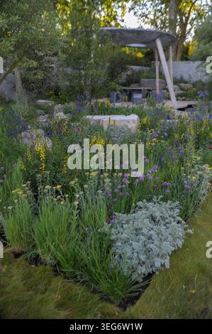 Eröffnungstag der Royal Horticultural Society Chelsea Flower Show 2023 - einer der Ausstellungsgärten: Das Eden Project: Bring Me Sunshine Garden. Dieser Garten ist von der Landschaft und Gemeinschaft der Morecambe Bay inspiriert und zelebriert Regeneration, Hoffnung und die Kraft junger Erwachsener, eine bessere Zukunft zu schaffen. Ein solarbetriebener Unterstand/Klassenzimmer mit geschwungenem Dach beherbergt Workshops, die Handwerkskunst, Gartenbau und digitales Lernen auf einer von Muscheln inspirierten Terrasse in einem reflektierenden Regenwasser-Recycling-Pool kombinieren. Eingerahmt von kalksteinhaltigen Materialien und salztoleranter Küstenwiesen-Pflanzung in Pin Stockfoto