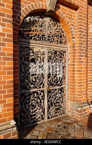 Kunstvolles schmiedeeisernes Tor in einem roten Backsteinbogen. Marias Kirche Stockfoto