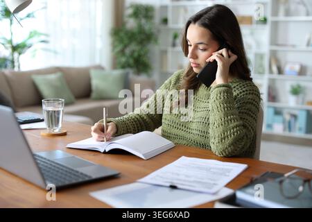 Telearbeiter, der telefonisch telefoniert und sich auf die Tagesordnung einlässt, zu Hause arbeitet Stockfoto