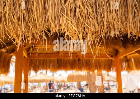 Blick aus der Nähe auf das Strohdach im Strandresort in Sharm El Sheikh Ägypten mit dem Urlaubsgebiet des Roten Meeres in weichem Fokus. Reise und Lebensstil im Resort. Stockfoto