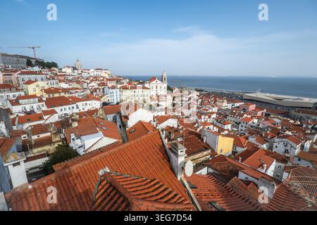 Panoramablick auf Lissabons historisches Viertel Alfama mit Terrakotta-Dächern, engen Gassen und Kirchen, die zum Fluss Tejo hinaufragen. B Stockfoto