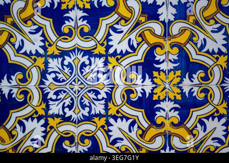 Dekorative portugiesische Azulejo-Keramikfliesen mit einem kunstvollen blauen und gelben Blumenmuster, die ein symmetrisches sich wiederholendes Motiv bilden, ideal für Inte Stockfoto