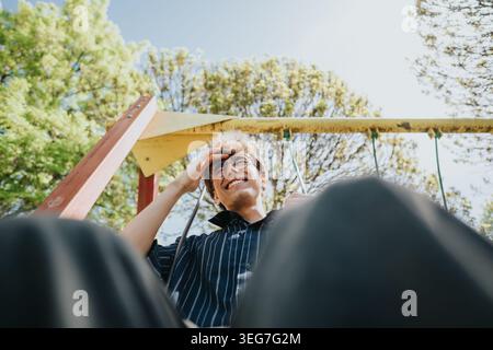 Junge Freunde, die einen sonnigen Nachmittag auf einer Spielplatzschaukel genießen, lächeln und sich im Park entspannen Stockfoto