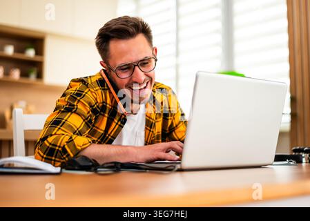 Der junge Mann arbeitet von zu Hause aus. Er benutzt Laptop und spricht über Smartphone. Stockfoto