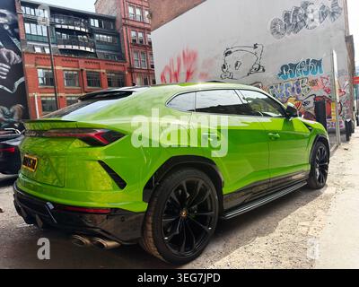 Manchester, UK - 01. Mai 2026: Lamborghini Urus aus hellem Kalk parkte neben Graffiti-bedeckten Backsteinhäusern in der Stadtstraße von Manchester UK. Stockfoto