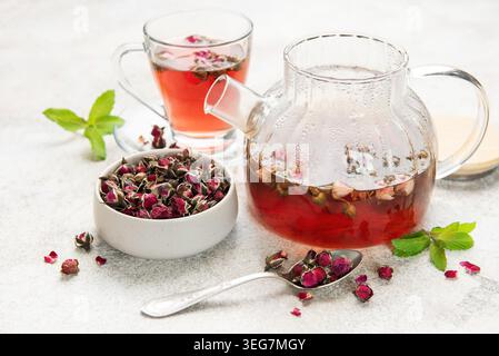 Rosentee in einer Teekanne aus Glas und Tasse mit getrockneten Knospen und frischer Pfefferminze Stockfoto
