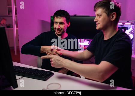 Zwei lächelnde Entwickler feierten erfolgreiche Teamarbeit und neue Projektvereinbarung am Schreibtisch, wobei die Computereinrichtung in sichtbar ist Stockfoto