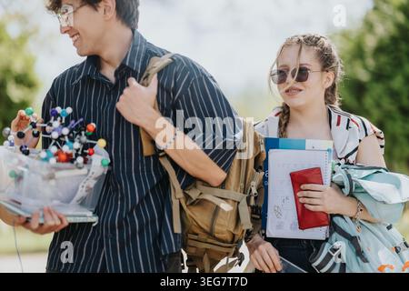 Zwei lächelnde Schüler mit Rucksäcken und Schulutensilien, während sie draußen spazieren Stockfoto