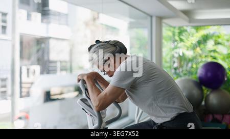 Ältere asiatische Frau, die sich müde fühlt, nachdem sie auf einem Fitnessgerät im Fitnessstudio trainiert hat Stockfoto