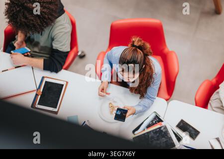 Junge Profis, die eine Pause mit Snacks und Geräten an einem ungezwungenen Arbeitsplatz machen Stockfoto