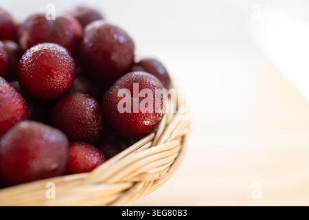 Frische Governor's Plum Flacourtia Indica Rote exotische Beeren im Korb mit Copy Space auf weiß Stockfoto
