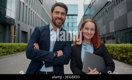 Kaukasische selbstbewusste Geschäftsfrau Mann mit Blick auf die Kamera lächelnd posierte in der Stadt erfolgreiche glückliche Geschäftsleute Hände überquerten das Außengebäude Stockfoto