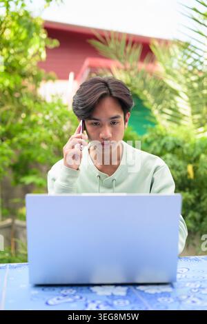 Ein vertikales Lifestyle-Porträt eines ernsthaften jungen asiatischen Geschäftsmannes oder Arbeitnehmers aus der Region Isan in Thailand, der draußen an einer blauen Kachel sitzt Stockfoto