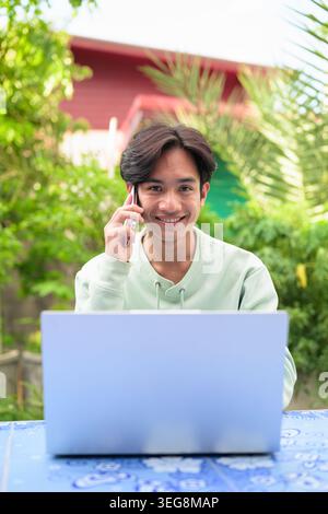 Ein vertikales Lifestyle-Porträt eines fröhlichen jungen asiatischen Kundendienstmitarbeiters oder Außenarbeiters aus der Region Isan in Thailand, der außerhalb sitzt Stockfoto