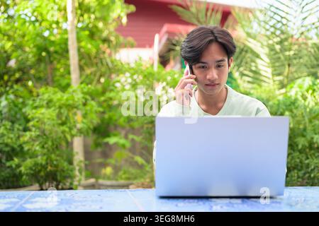 Ein horizontales Lifestyle-Porträt eines ernsthaften jungen asiatischen Kundenbetreuers oder eines externen Mitarbeiters aus der Region Isan in Thailand, der draußen sitzt Stockfoto