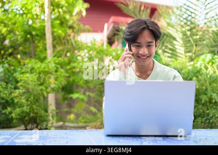 Ein horizontales Lifestyle-Porträt eines fröhlichen jungen asiatischen Kundendienstmitarbeiters oder eines externen Mitarbeiters aus der Region Isan in Thailand, der Sie sitzt Stockfoto