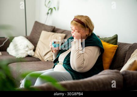 Emotionale ältere Frau, die Tränen abwischt, während sie auf der Couch sitzt. Stockfoto