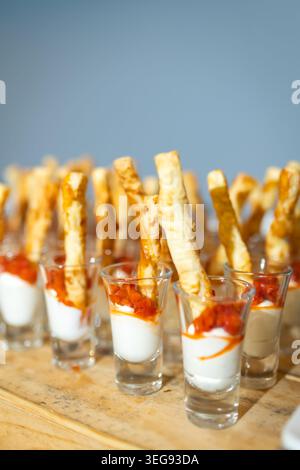Goldene Brotstäbchen tauchen in cremigen Weißkäse mit leuchtendem rotem Kaviar in klaren Gläsern. Stockfoto