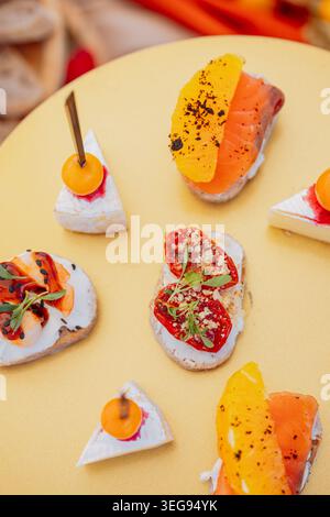 Elegante Vorspeisen mit Räucherlachs, Kirschtomaten, frischen Kräutern und Frischkäse, die kunstvoll auf einer leuchtend gelben Oberfläche angeordnet sind Stockfoto