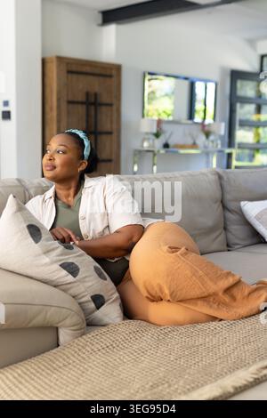Afroamerikanische Frau, die sich auf einem Sofa im Wohnzimmer liegend und auf gemusterten Kissen ruht Stockfoto